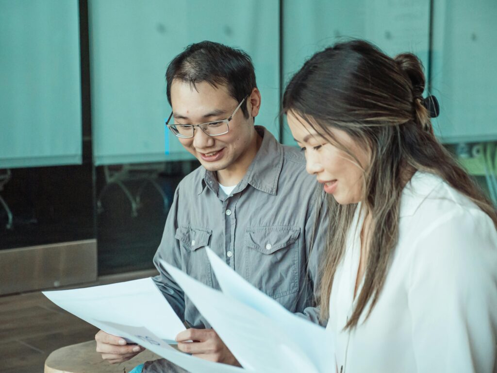 Two colleagues review documents together in a modern office setting, promoting teamwork and collaboration.