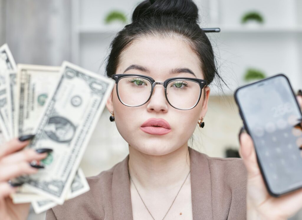 pexels-photo-7735790-7735790 Portrait of a businesswoman holding cash and smartphone, emphasizing financial management and success.